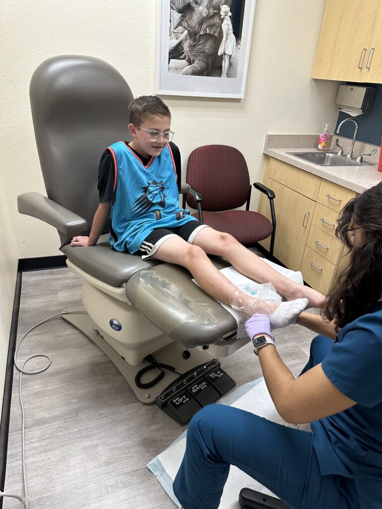 Image of a boy sitting on the patient chair in clinic being casted for his orthotic by a certified medical assistant