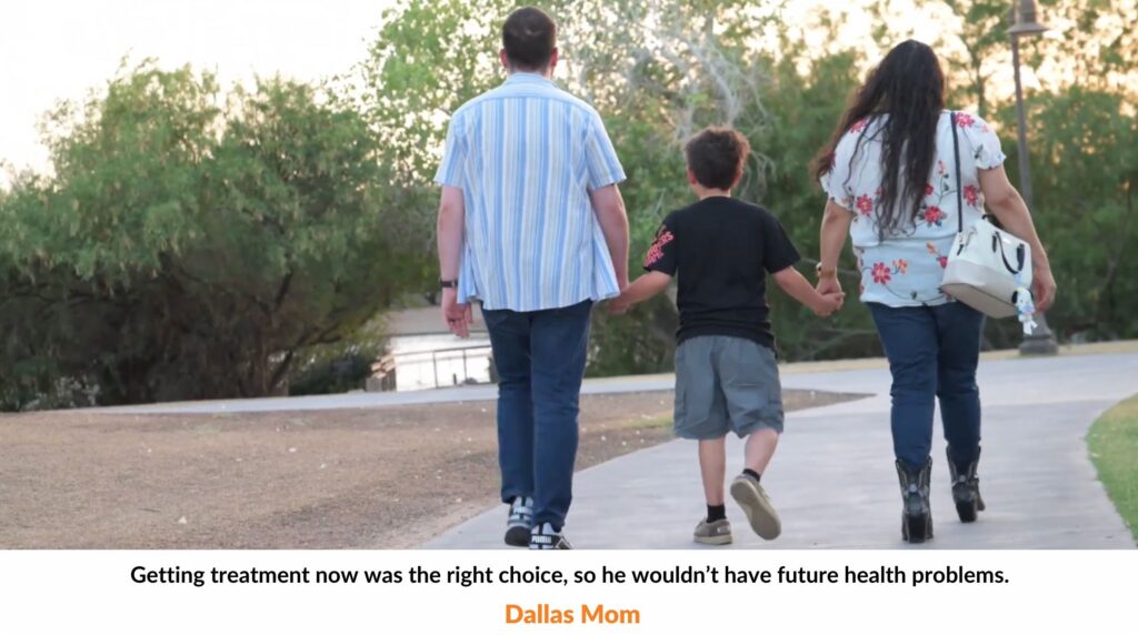 image of boy walking down in the park with his parents holding hands towards the sunset